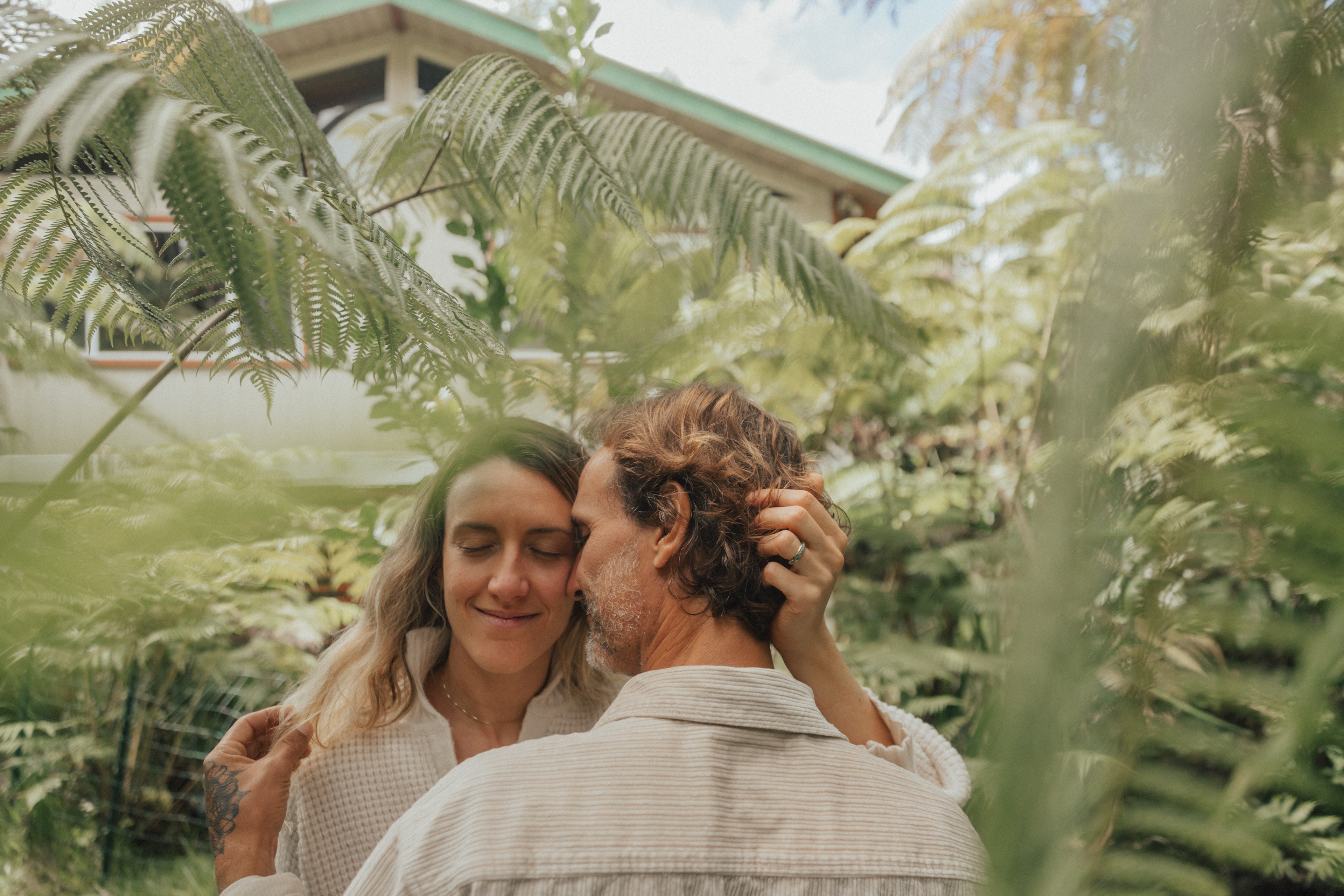A couple embracing among giant ferns, her eyes closed, smiling