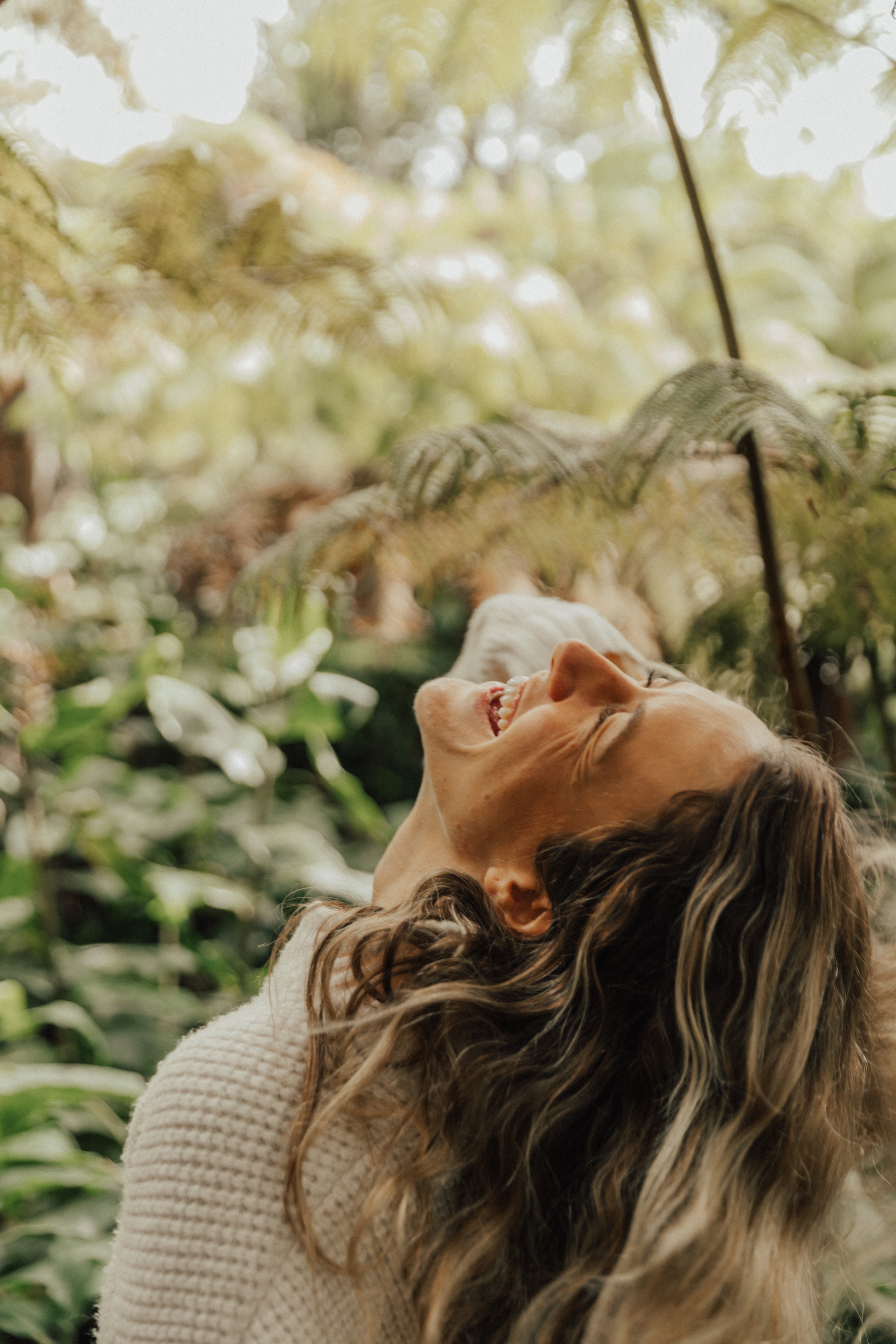 A woman laughing with her head thrown back among the ferns